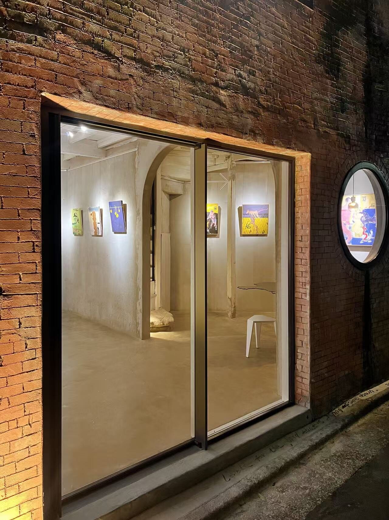 Xuanwu Art Space at night — the lit gallery and hung works seen through the window